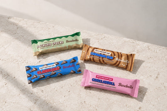 Four Barebells protein bars in colorful wrappers arranged on a light stone surface.