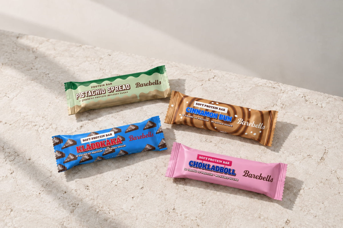 Four Barebells protein bars in colorful wrappers arranged on a light stone surface.
