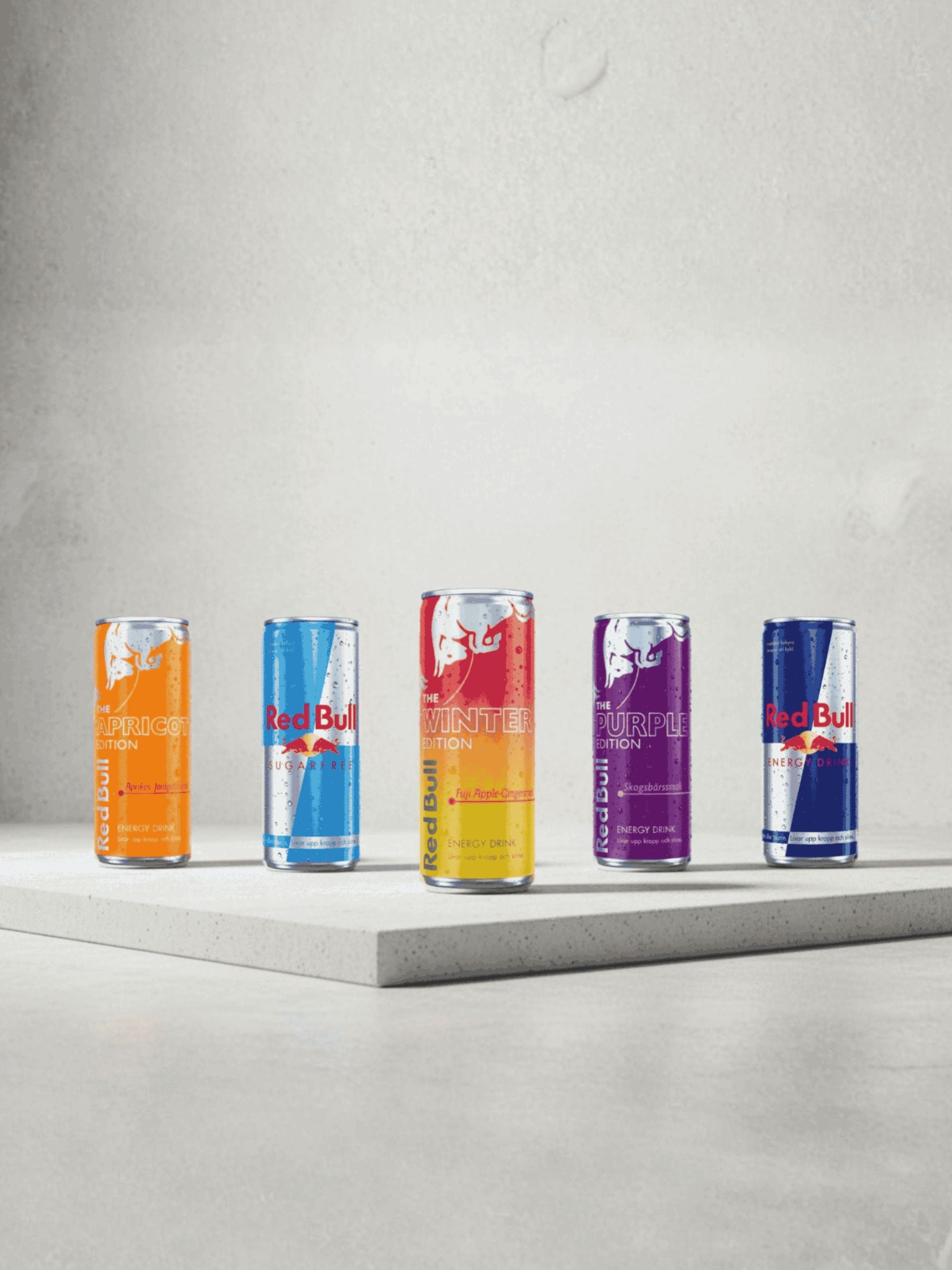 Five Red Bull energy drink cans in different flavors on a gray surface with a light gray background.