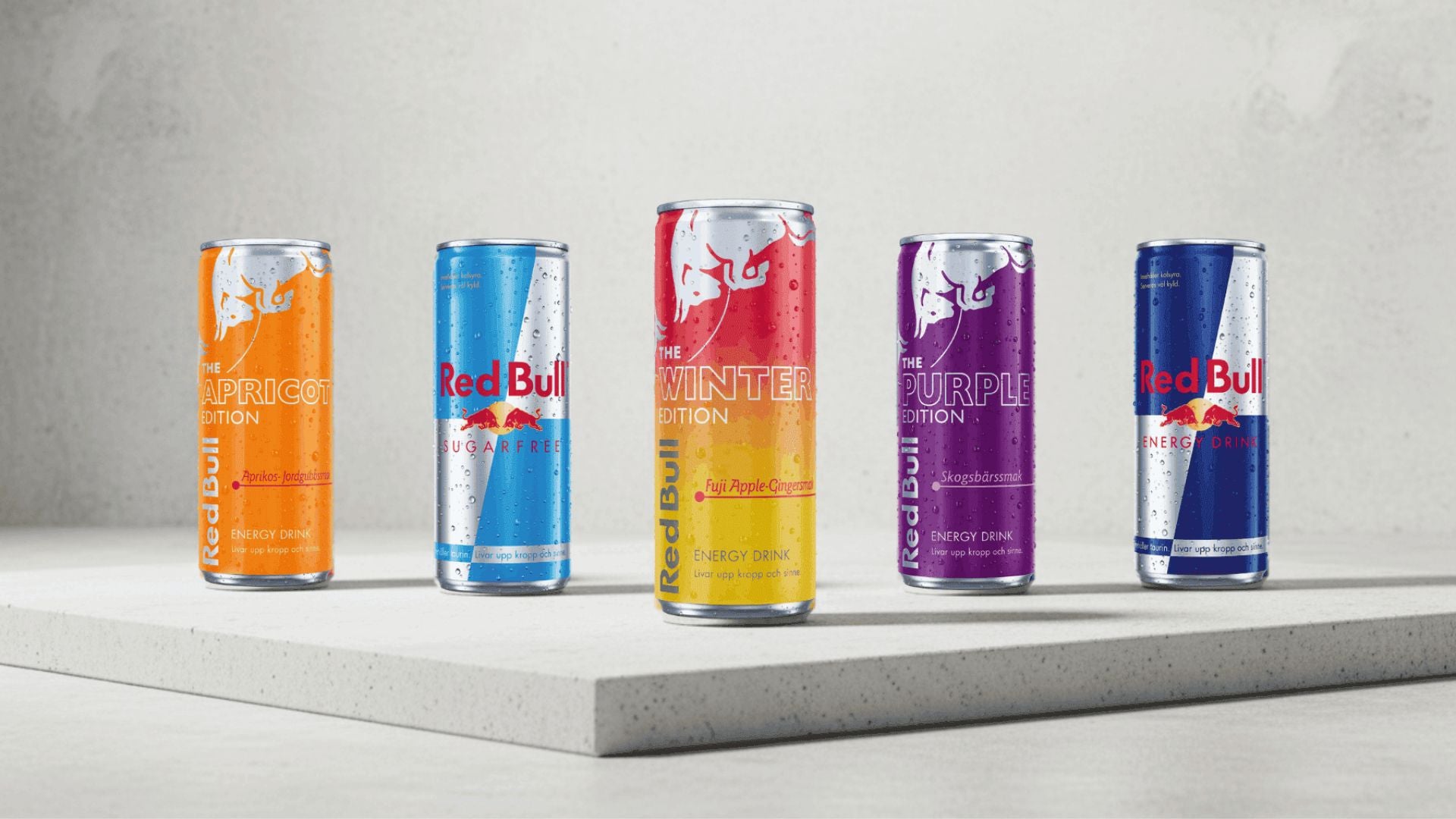 Five Red Bull energy drink cans in different flavors on a gray surface with a light gray background.